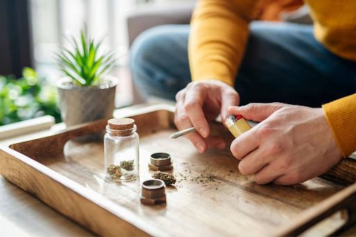 Person preparing a cannabis joint from a glass jar on a wooden tray, illustrating one of the methods to consume THCa flower.